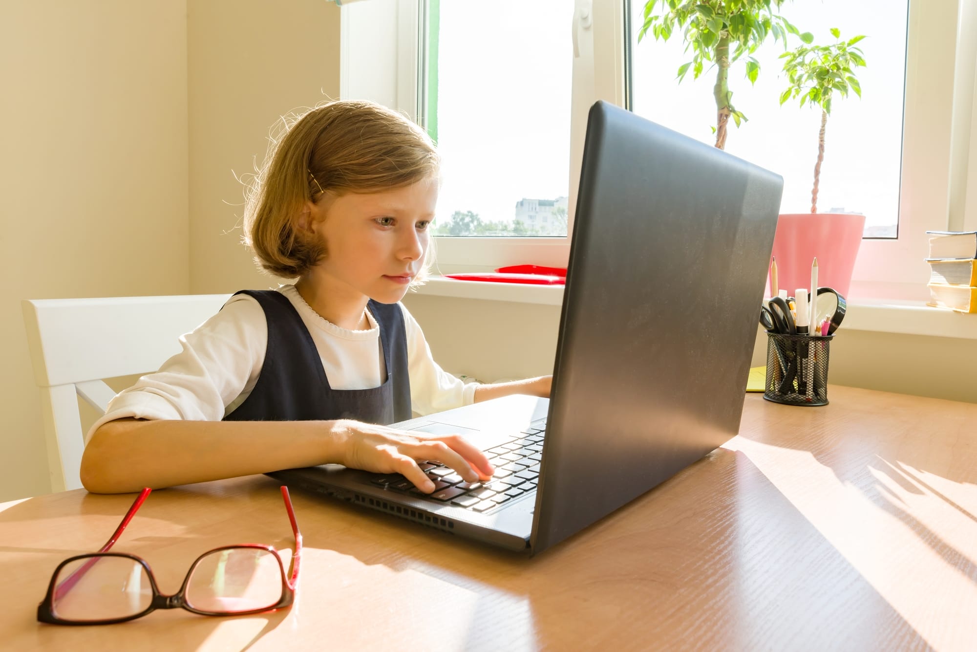 Little schoolgirl uses computer sitting at a desk at home. School, education, knowledge and children.
