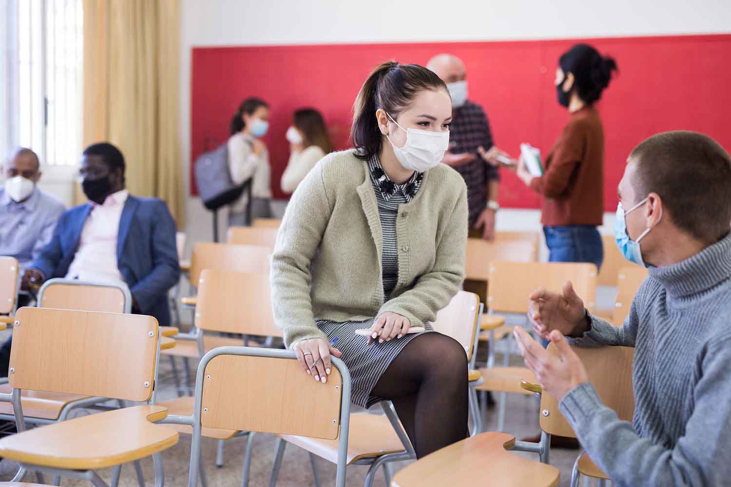 Students in protective masks are talking about homework at desk